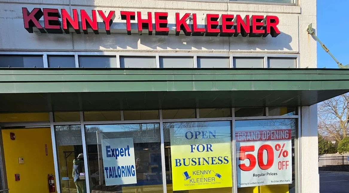 Storefront with signs reading "KENNY THE KLEENER," "Expert TAILORING," "OPEN FOR BUSINESS," and "GRAND OPENING 50% OFF Regular Prices.