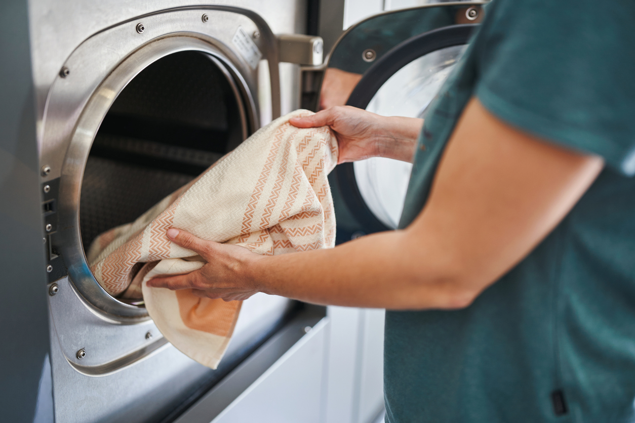 Person loading a patterned towel into a front-loading washing machine, with the door open and their hands holding the fabric.